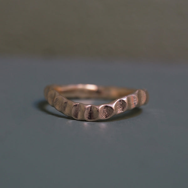 Curved beaten stacking ring in yellow gold, shaped to sit flush against an engagement ring